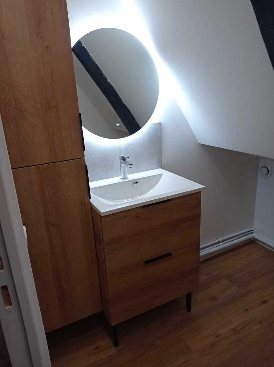 Une salle de bain design avec un miroir rond lumineux au dessus du meuble vasque